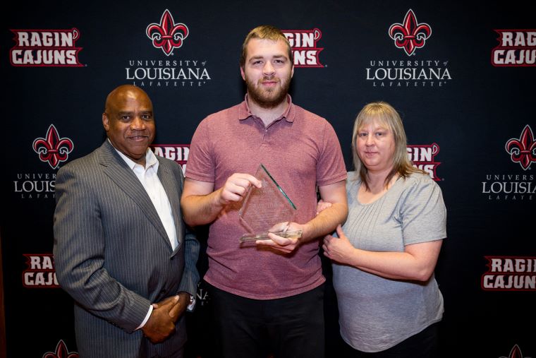 An LEP student holding an award, poses with his mother and Dr. DeWayne Bowie