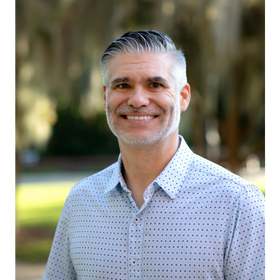 Headshot: Scott Sittig is pictured outdoors wearing a patterned button-down shirt. 
