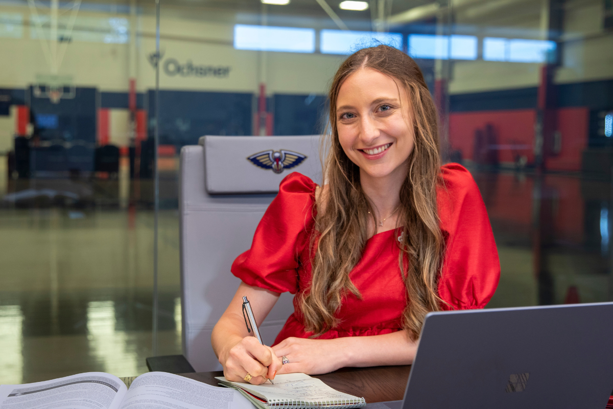Alumni of the sport management degree program works at computer in the New Orleans Pelicans' practice arena.
