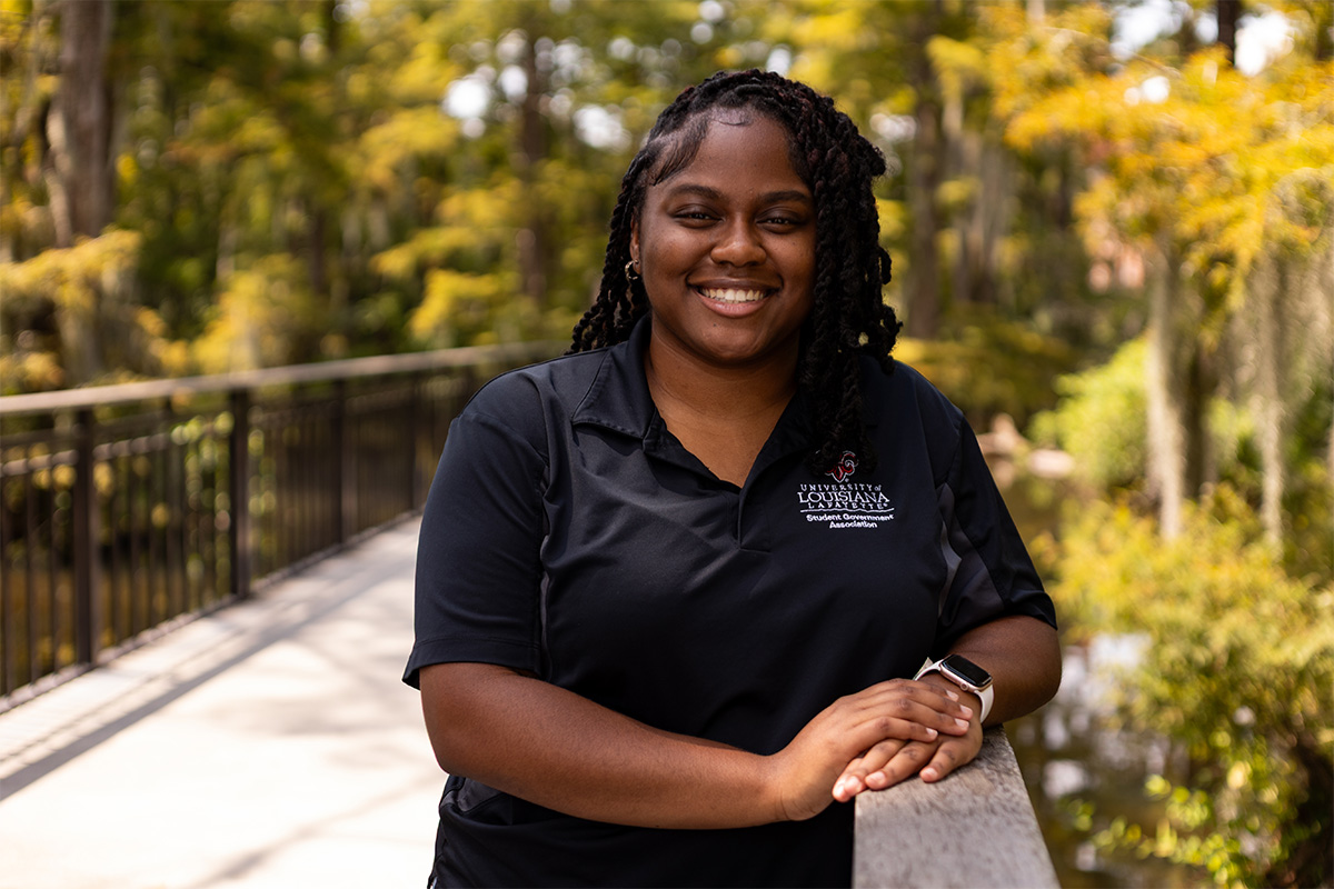 Onyeka Nwaezeapu smiling and wearing a student government association polo, standing near the UL Lafayette swamp.