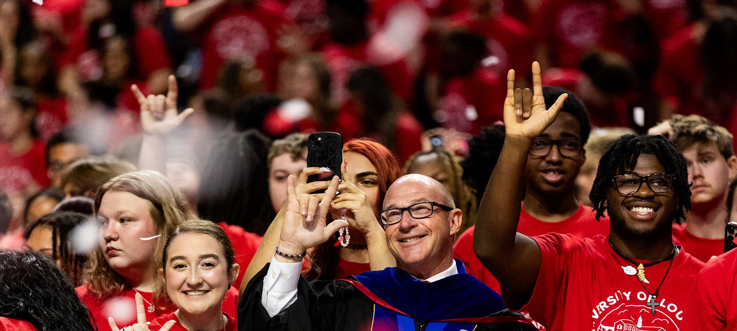Dr. Jaimie Hebert makes the UL hand symbol surrounded by students at Convocation