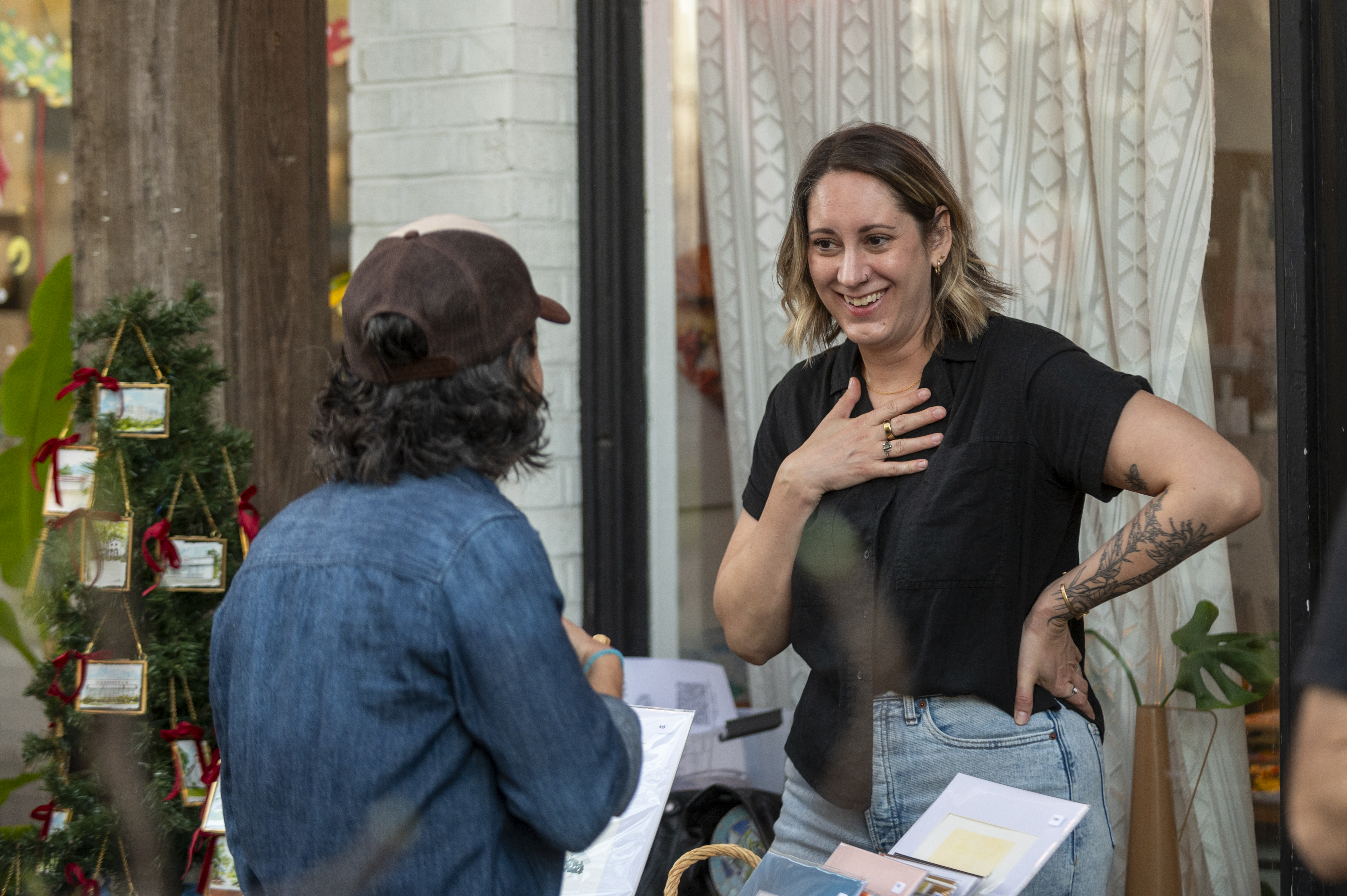 Lindsey Croall wears a black blouse and holds one of her watercolor illustrations while talking with a patron during an ArtWalk event.