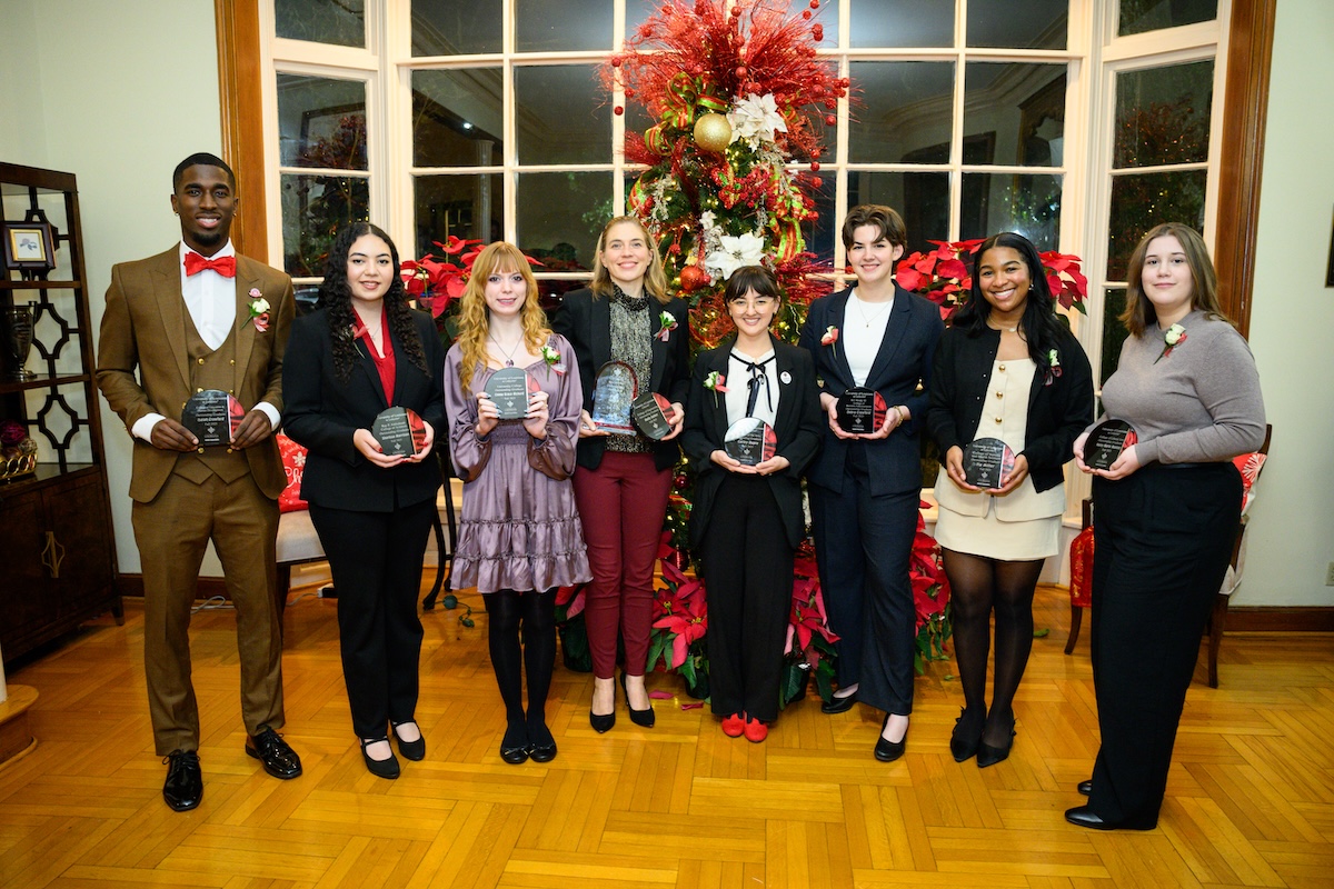 Eight Outstanding Graduates stand in front of a Christmas tree holding awards.