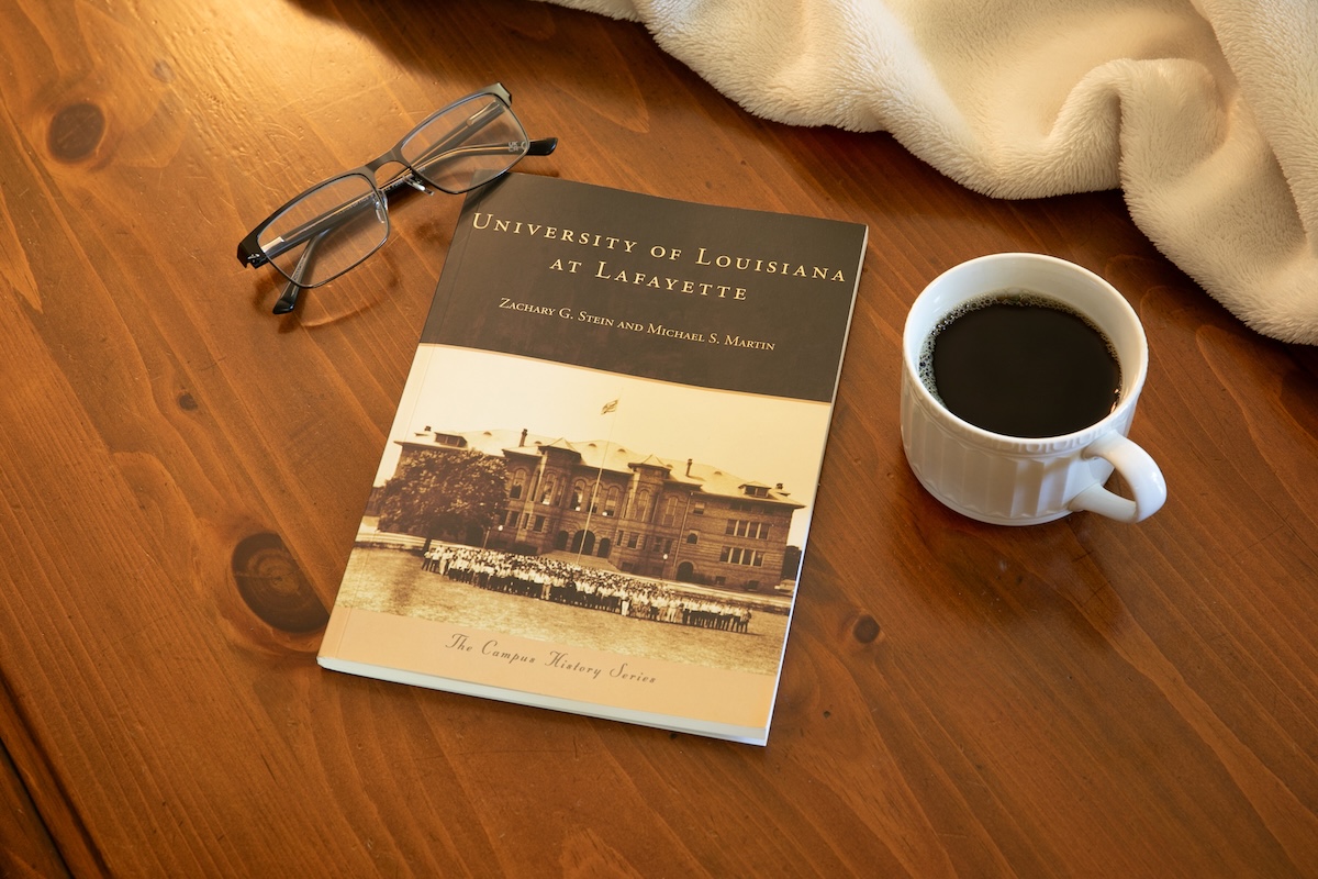 A book on a table with glasses and a cup of coffee.