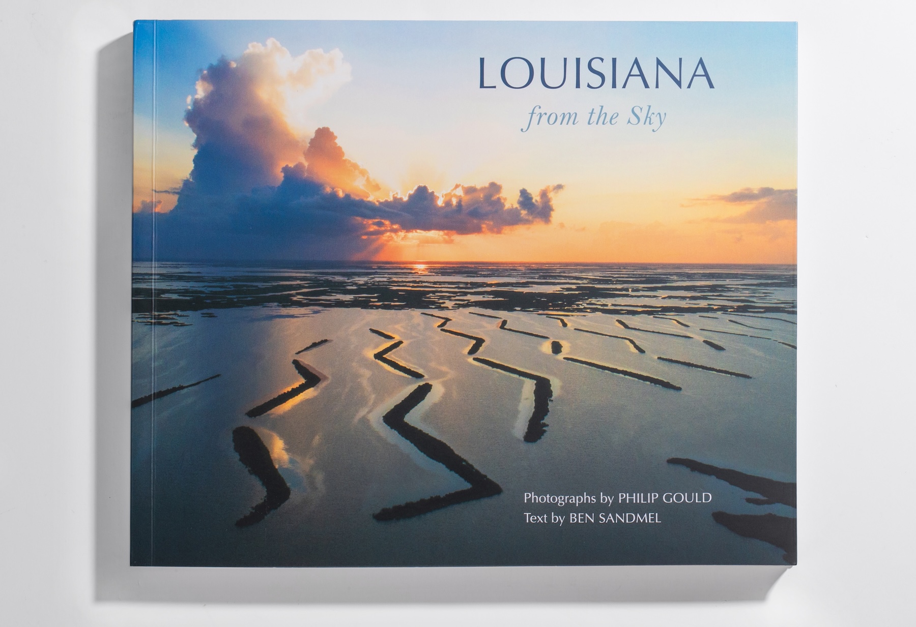The cover of the book "Louisiana from the Sky" featuring an aeriel view of a flooded landsape and a setting sun through the clouds.