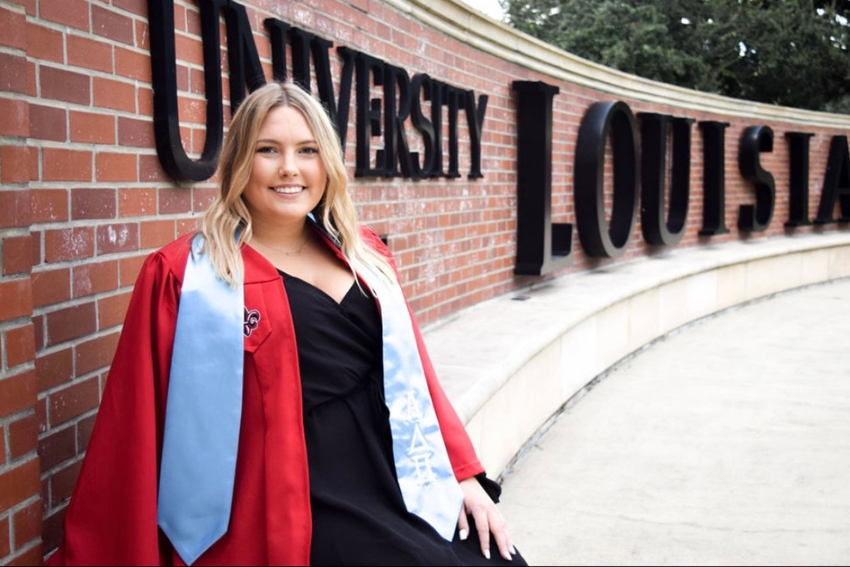 Online MGMO graduate smiles in front of UL Lafayette sign.