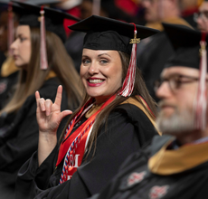 MBA online graduate smiles at UL Lafayette's Commencement Ceremony, throwing up the Ragin' Cajun hand sign.