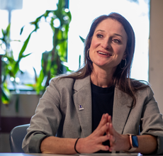 An HR manager speaks in an office, wearing a black top and gray blazer.