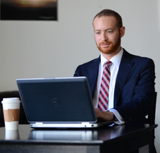 UL Lafayette student studies on laptop during lunch break, wearing a navy suit and tie. 