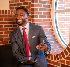 Online MBA grad smiles in a gray suit and tie while consulting. 