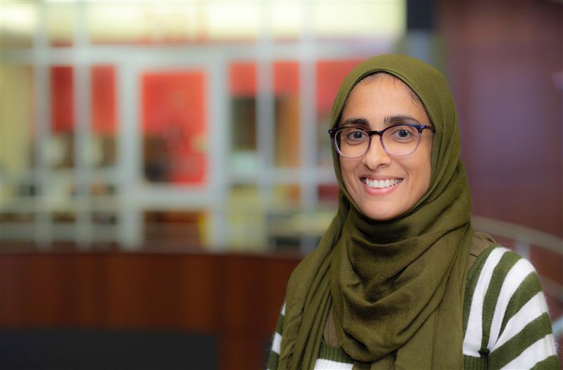 Dr. Beenish Chaudry is pictured indoors wearing a green striped shirt and green hijab.