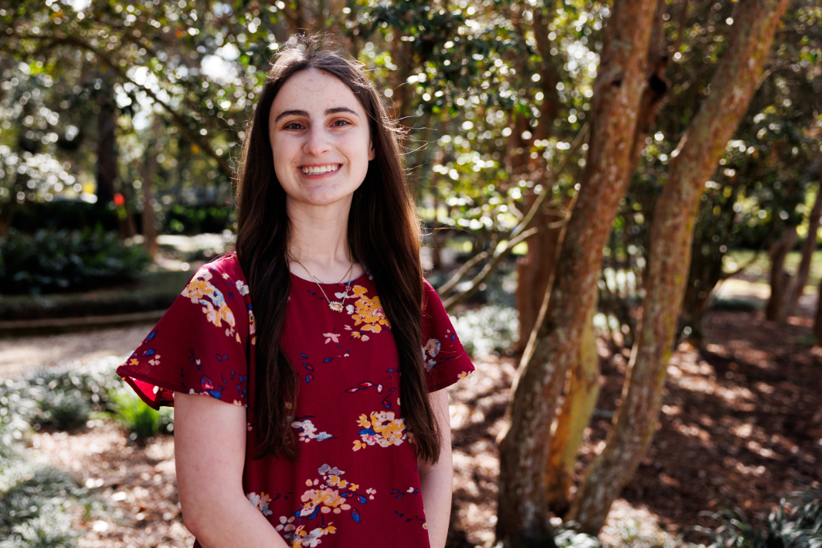 Portrait photograph of Bree Landry smiling in a burgundy blouse with a nature background.