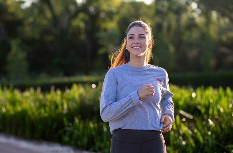 Sport management online student smiles on an outdoor run, wearing a gray UL Lafayette t-shirt. 