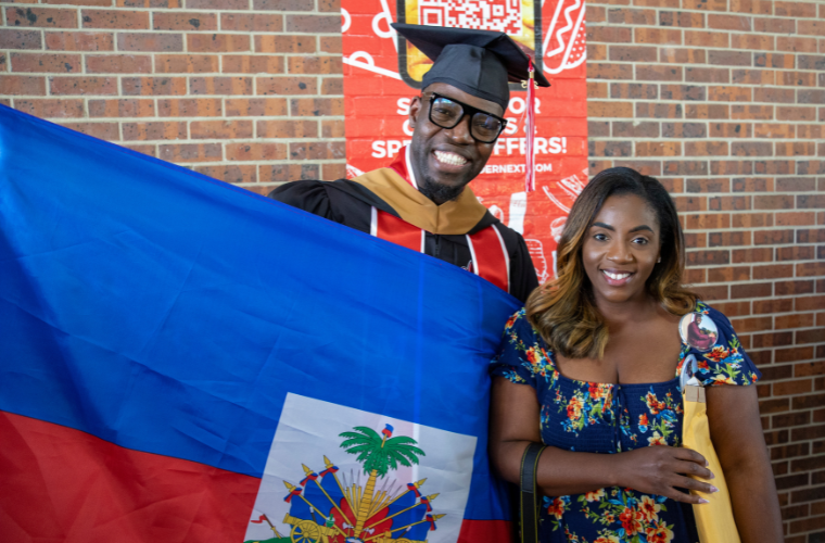 Global Management MAB online graduate smiles at commencement ceremony holding a flag.