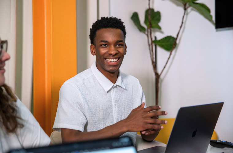 General studies online graduate smiles while collaborating with his team in a conference room. 