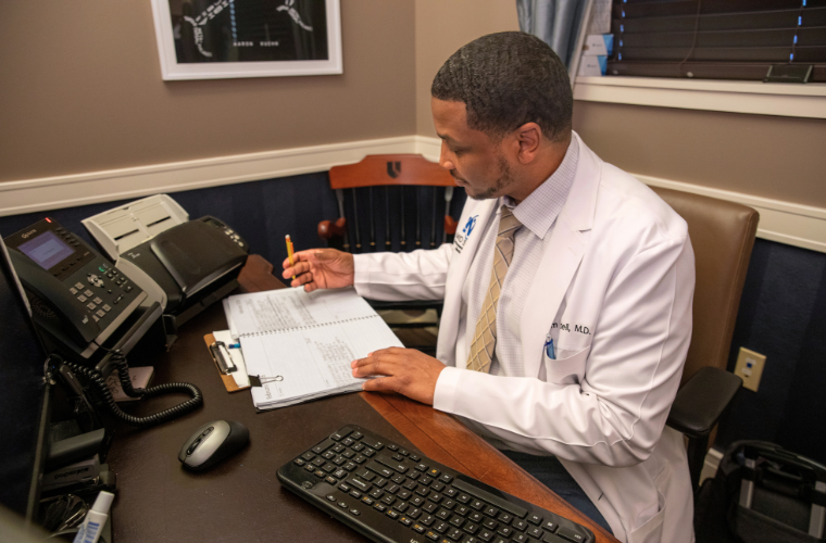 Health Care Administration online MBA graduate fills paperwork, wearing his white physician coat. 