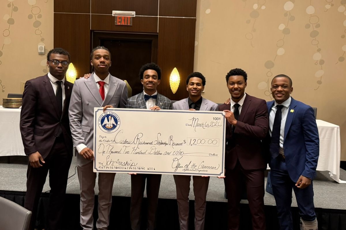 Six collegiate men hold up a giant check in the amount of $1,200.