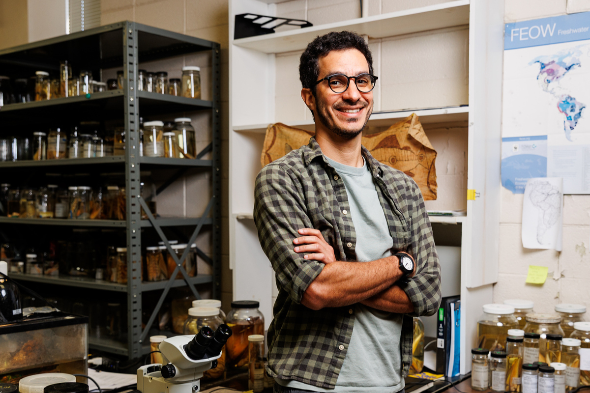 Portrait photo of Jesse Filho smiling with his arms folded wearing glasses, a gray t-shirt, a flannel button down and watch.