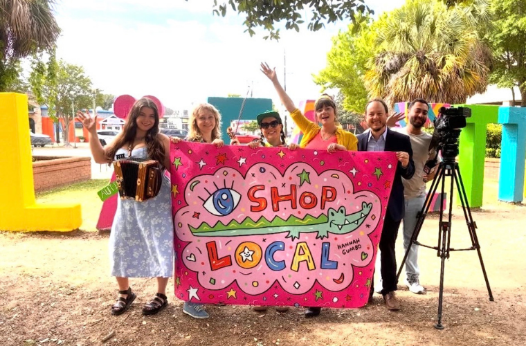 Six people hold up a pink banner that says Shop Local
