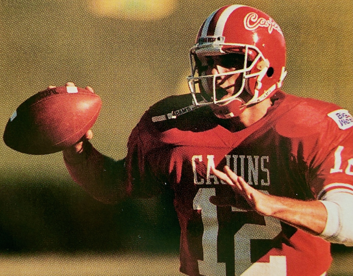 In this archive photo Cajuns quarterback Jake Delhomme wears a red jersey and helmet with a football in hand.