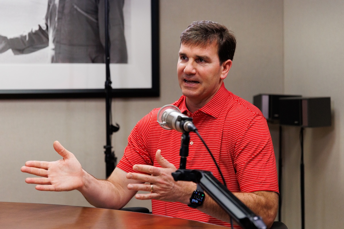 Jake Delhomme is wearing a red shirt sitting at a desk with a microphone.