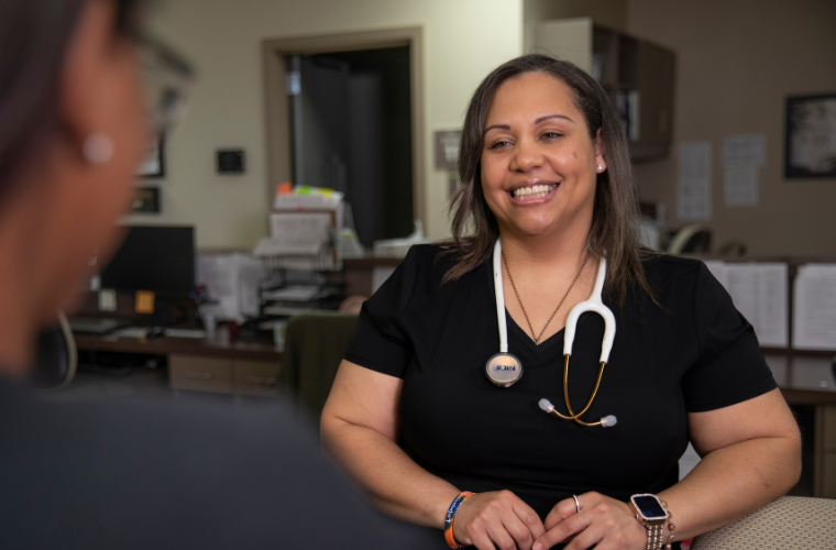 Online RN to BSN graduate smiles while collaborating with fellow medical staff.