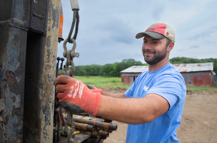 Engineering Management online grad smiles while working on water drilling equipment. 