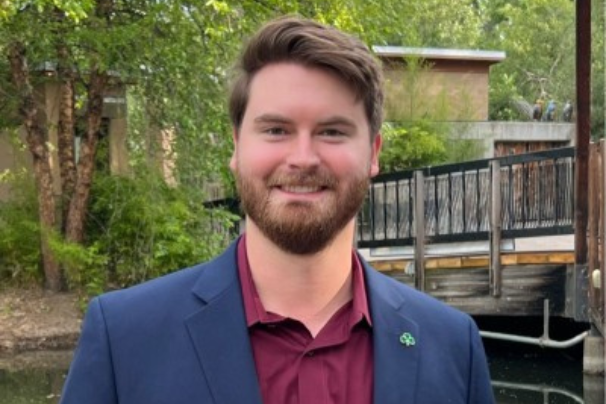 Online MBA in Finance alumni smiles in a maroon collared shirt and navy sports coat. 