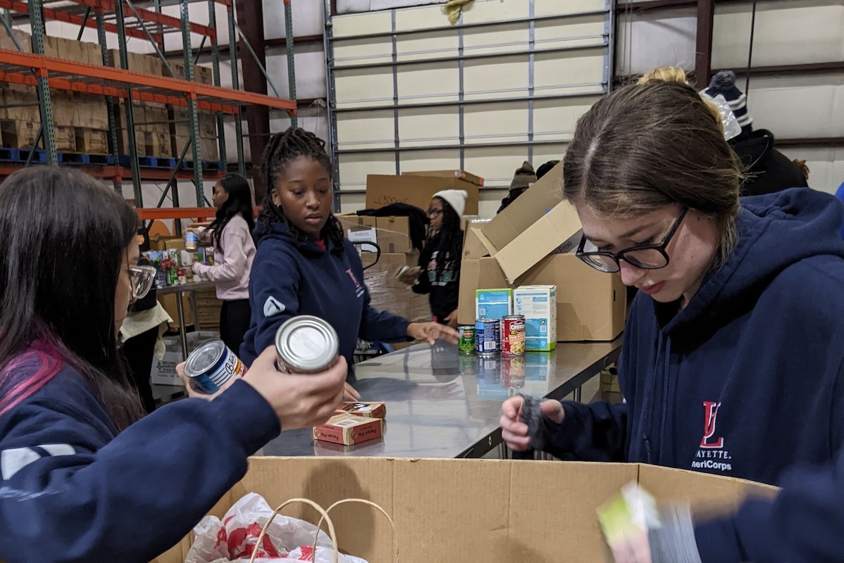 Three students in blue hoodies sort canned goods at a Second Harvest warehouse.