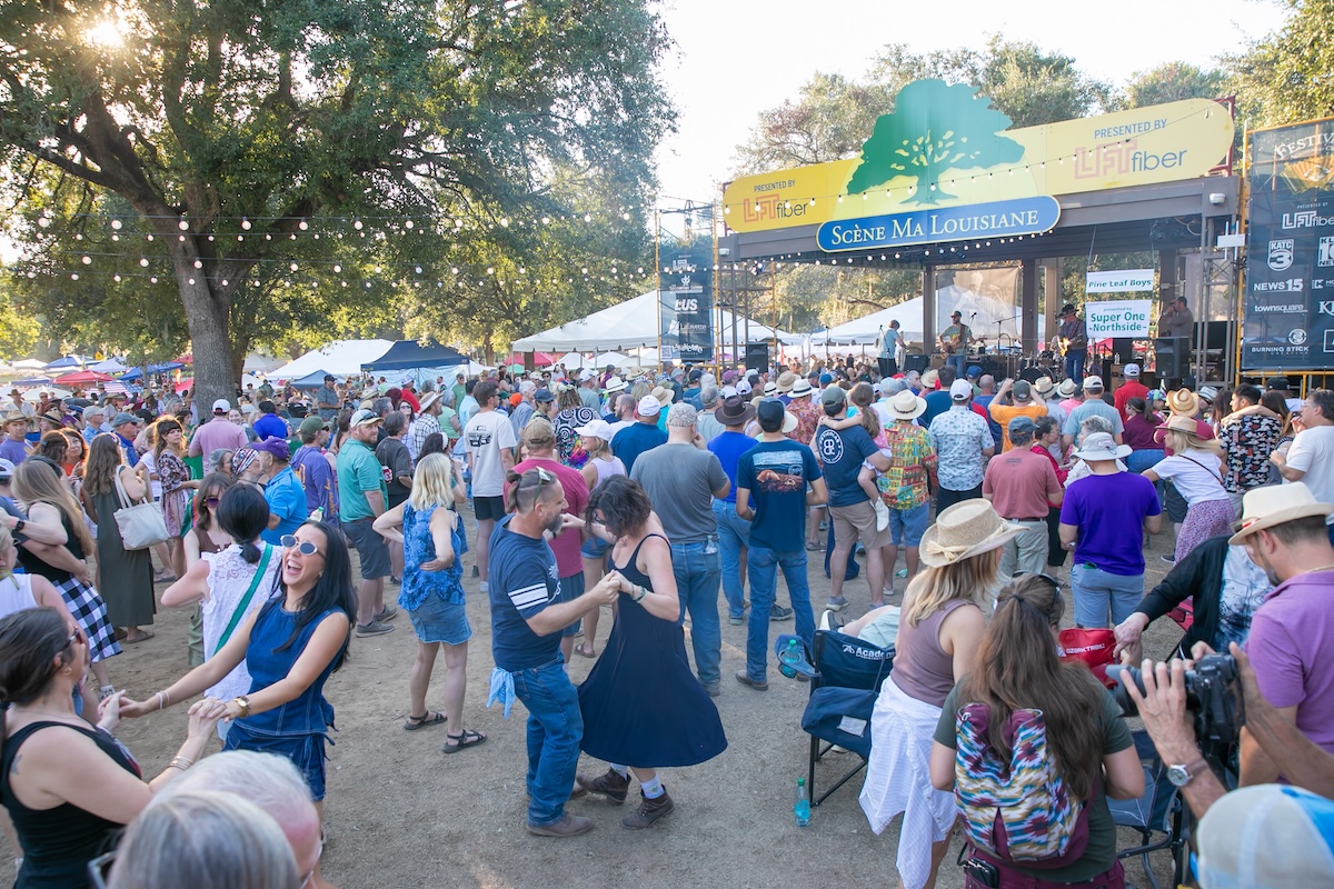A crowd of people dance on an outdoor dance floor with a stage in the background.