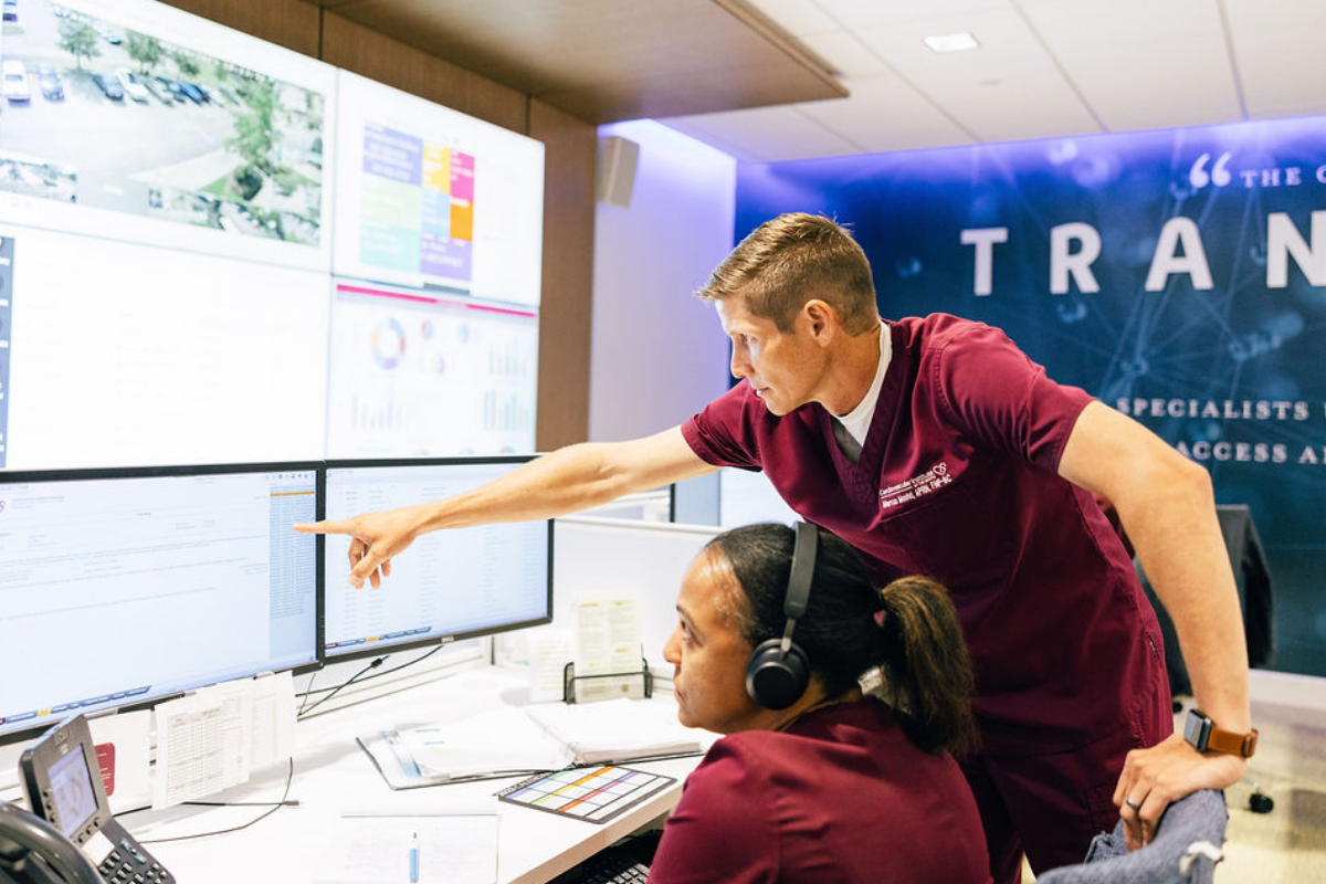 Graduate of the online MBA program points to computer screen, wearing maroon scrubs.