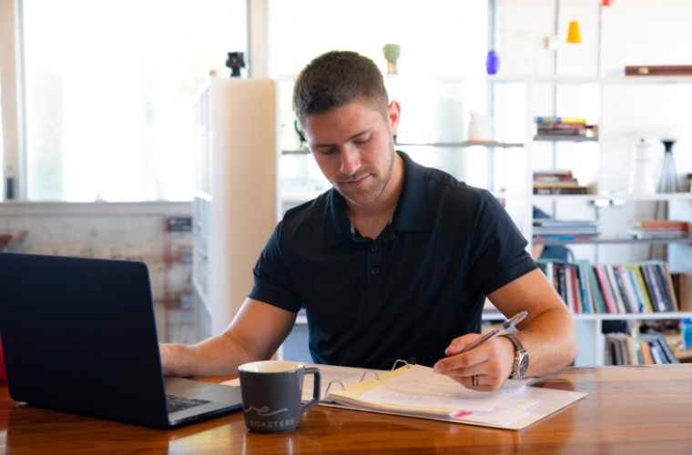 UL Lafayette student working at a coffee shop with his laptop and notepad.