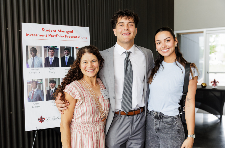 Students standing in front a presentation board titled Student Managed Investment Portfolio Presentation.