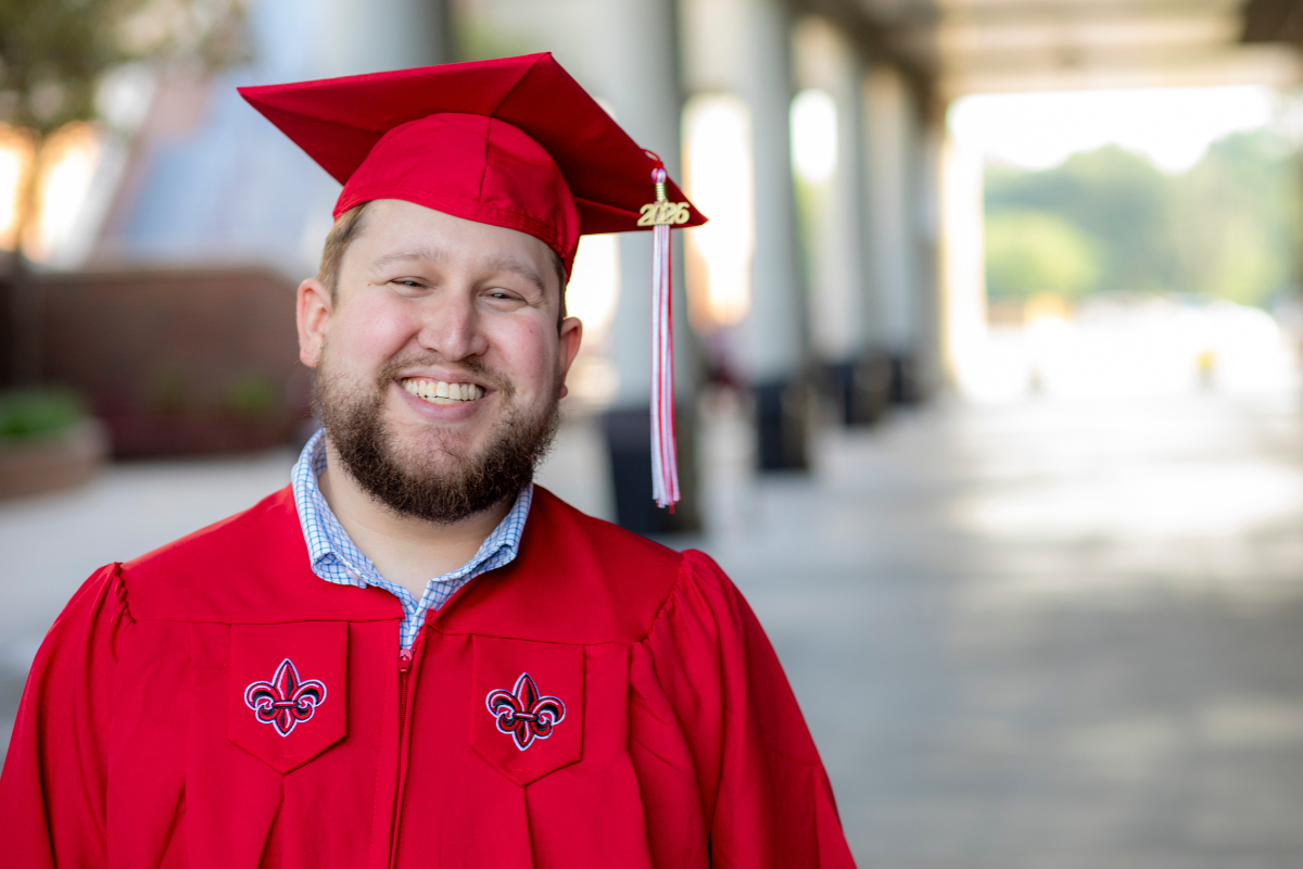 Graduate of the online management bachelor's degree program smiles in his cap and gown after graduating.