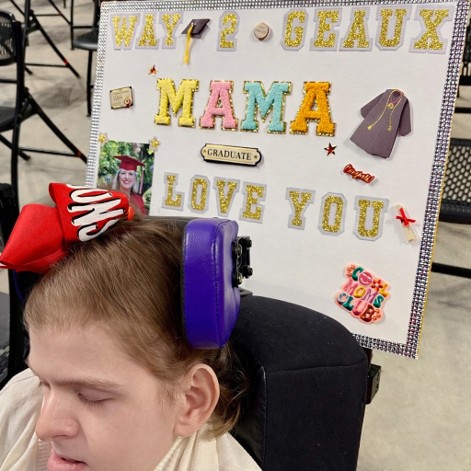 Lexi Baudoin at her mother's graduation in 2025, a homemade sign placed behind her. 