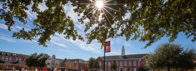 Students walk through campus quad and sit at center fleur-de-lis fountain framed to the left