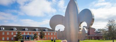 Fleur de lis statue in the UL Lafayette campus quad with the Maraist Financial Services Lab behind
