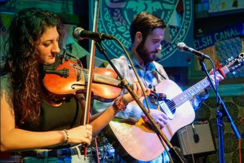 A woman playing the Cajun fiddle and a man playing the guitar on a stage