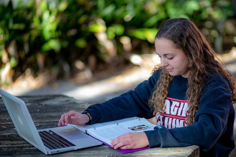 University of Louisiana at Lafayette student in a Ragin' Cajuns sweatshirt working on a laptop outside