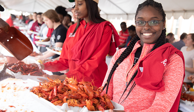 UL Lafayette student in a red pullover holding a tray of crawfish at Lagniappe Day