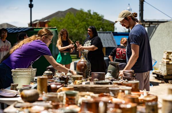 UL Lafayette students and community members surrounding tables covered in student ceramic works for sale.