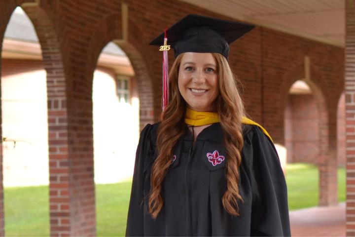 Tori Miguez, dressed in cap and gown, poses for a photo on UL Lafayette's campus.