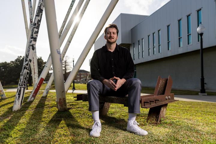 Professional photo of Christian Willis sitting down in front of the university's architecture.