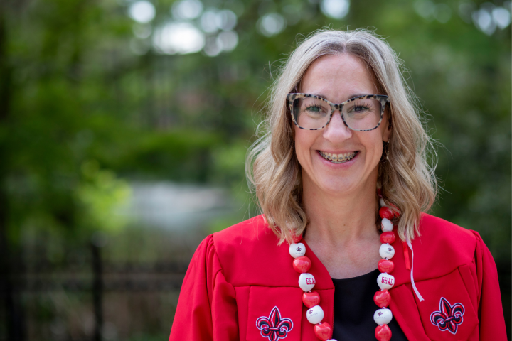 Stephanie Jacobs, graduate of the RN to BSN online program, poses for a photo in front of Cypress Lake, wearing her UL Lafayette cap and gown and a Ragin' Grad necklace.