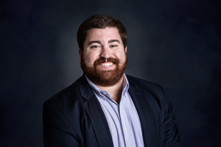 Graduate of UL Lafayette's MS in Accounting online program smiles for headshot in a blue button down and coat.