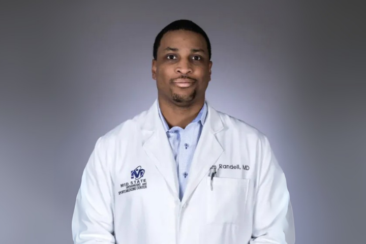 MBA in Health Care Administration online graduate smiles for headshot in white medical coat.