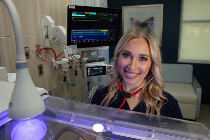 Graduate of UL Lafayette's online nursing program smiles while performing a NICU assessment.