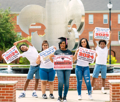 Bridget Terry smiles for photo with her four children, each holding a sign indicating when they will be graduating