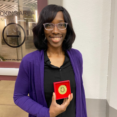 At UL Lafayette's Honors Convocation, Denise smiles and holds up the medal she received.