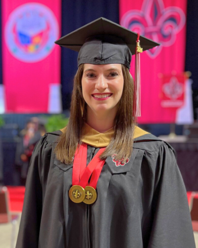 Kaley Carroll, wearing her master's regalia, smiles for a photo in front of the stage at UL Lafayette's Commencement.